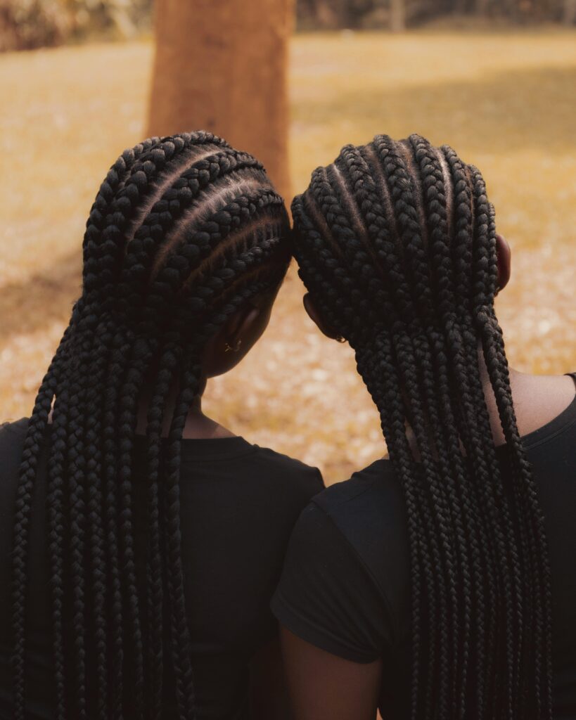 Two women with intricate braided hairstyles embracing outdoors in Abuja, Nigeria.